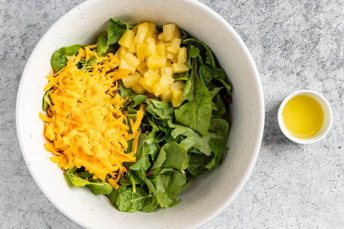 Taste of Home Hawaiian Salad recipe photo of combining the greens, fruit, and cheese in a mixing bowl.