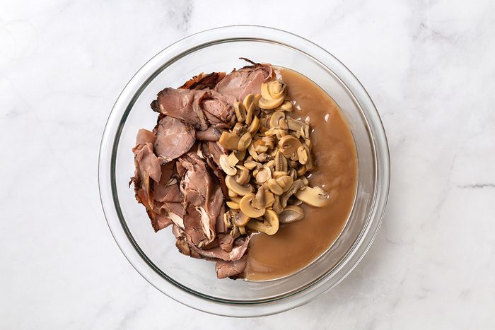 Sliced deli roast beef, beef gravy, sliced mushrooms in a mixing bowl for step one of Hot Roast Beef Sandwich Recipe for Taste of Home