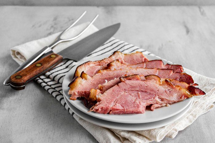 3/4th shot; white background; Smoked Ham served on white plate; knife and fork; kitchen towel;