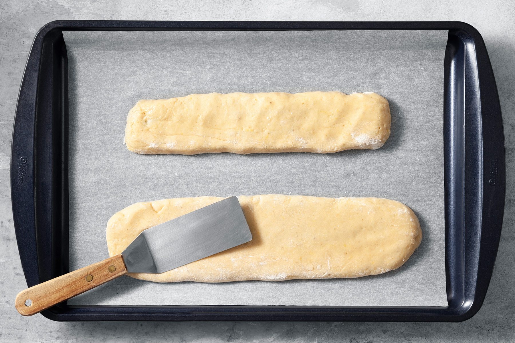 Overhead shot of transfer to a baking sheet lined with parchment; flatten to 1/2 inch thickness; flat spatula; bake until golden and tops begin to crack; grey marble surface;