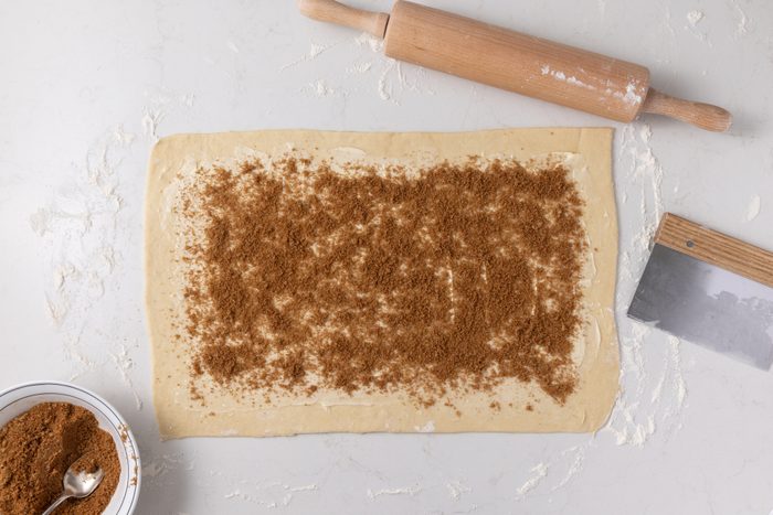 Dough being rolled and filled with cinnamon and sugar mixture.