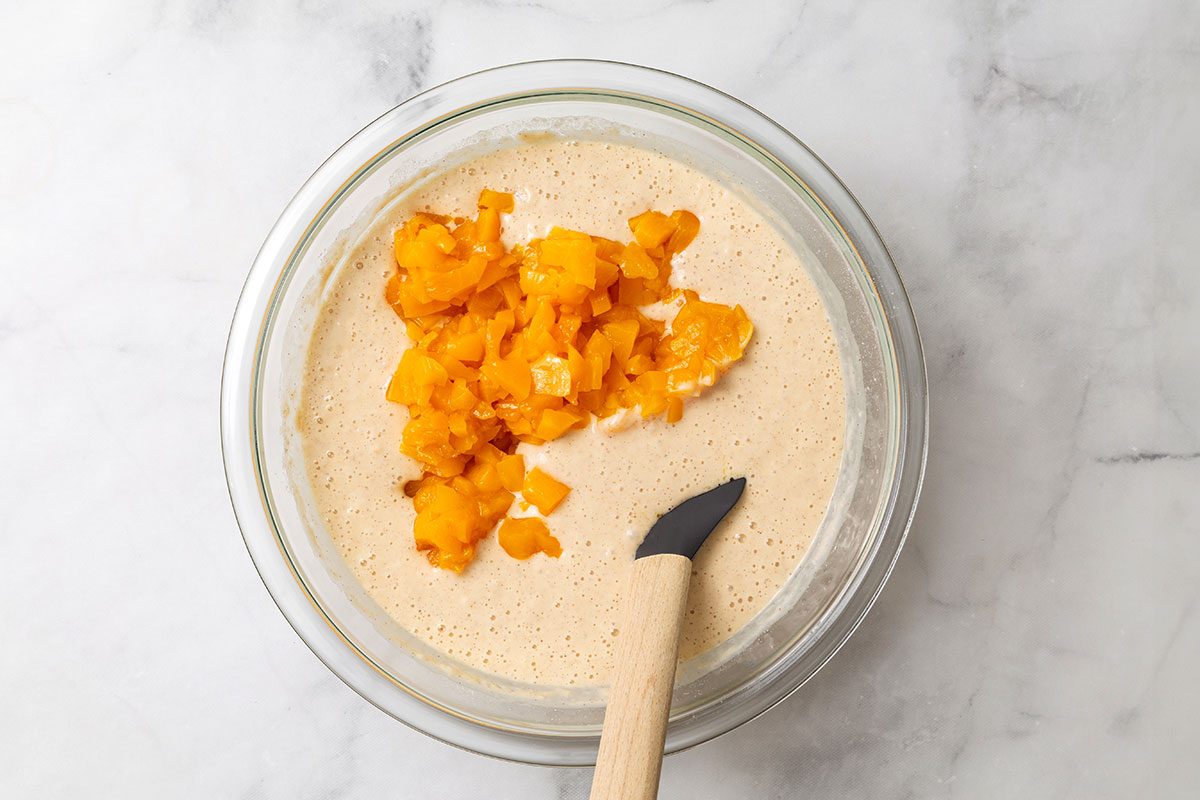 Finely chopped peaches being mixed with pancake batter in a mixing bowl