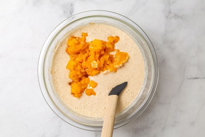Finely chopped peaches being mixed with pancake batter in a mixing bowl