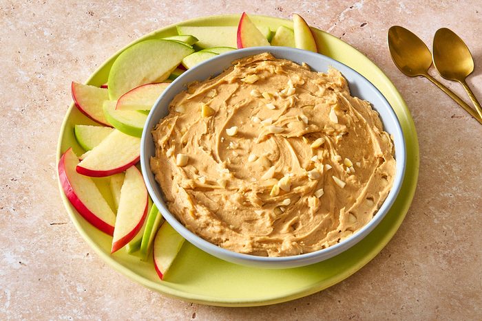 Angled shot of peanut butter dip served in a bowl, topped with some chopped peanuts and served with apple slices