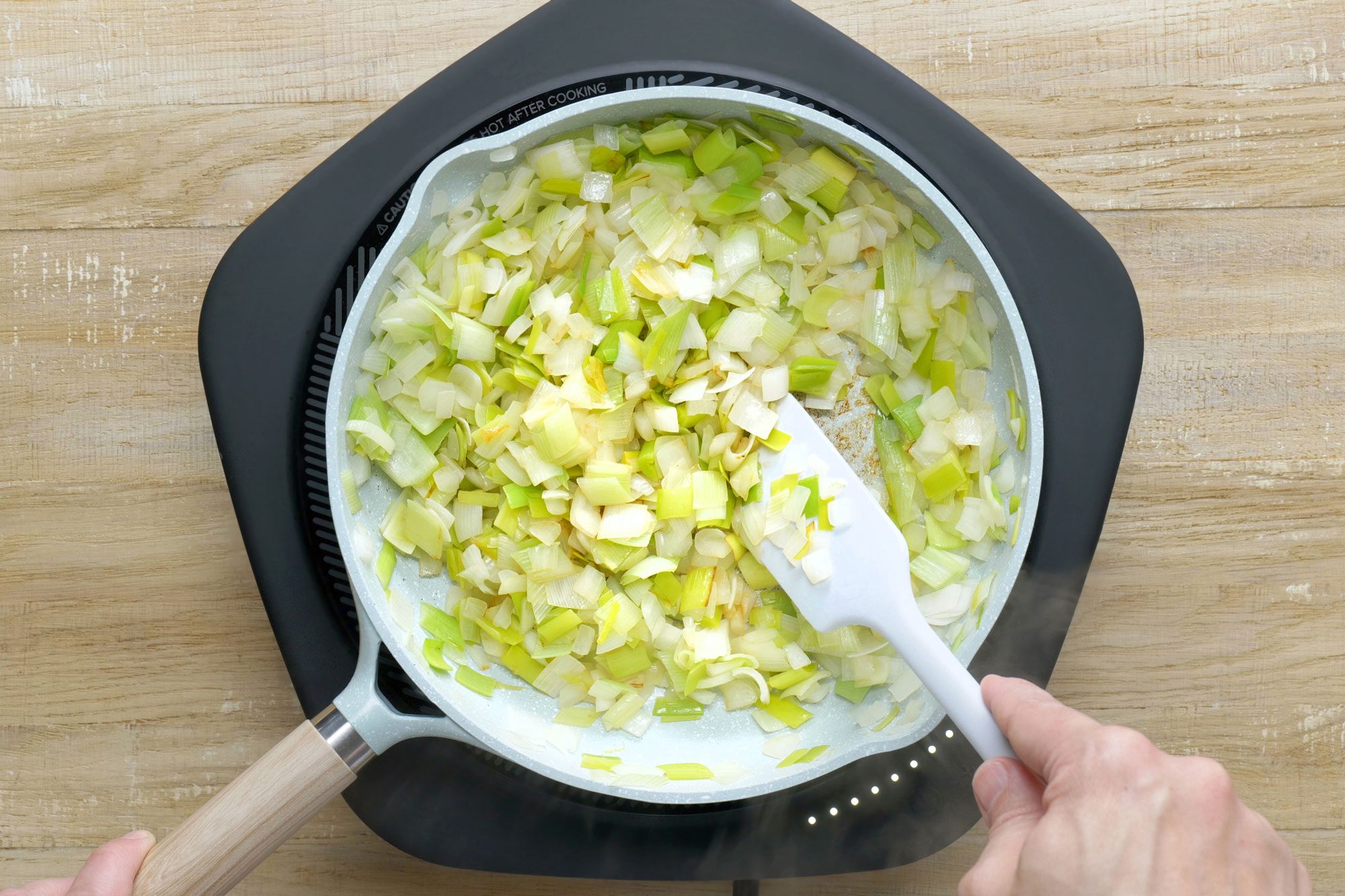 overhead shot; wooden background; In a lightly greased skillet, cooking leeks and onion;