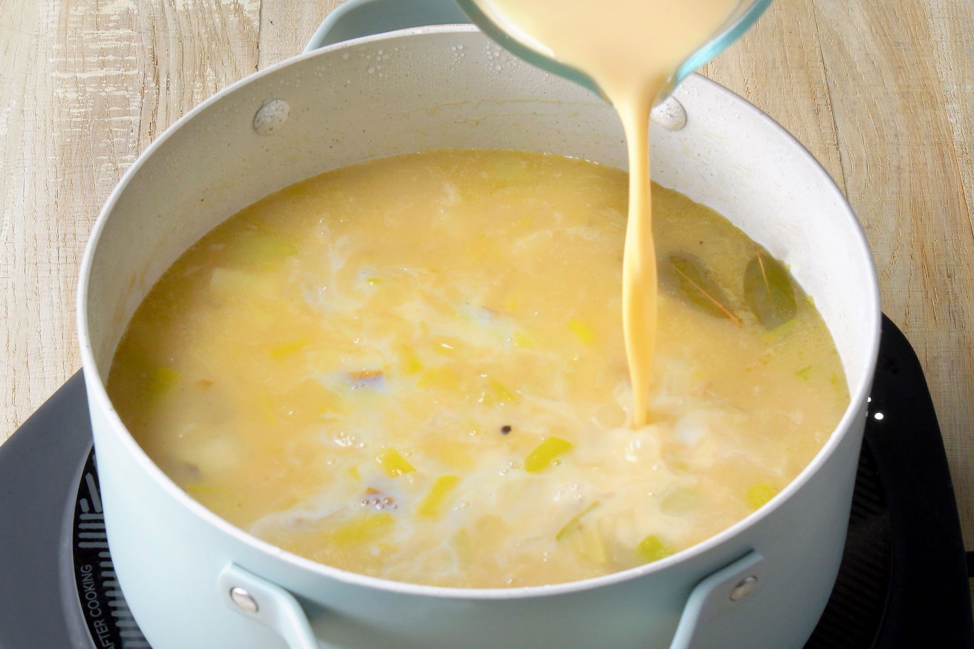 3/4th shot; wooden background; adding in milk and evaporated milk into the saucepan;