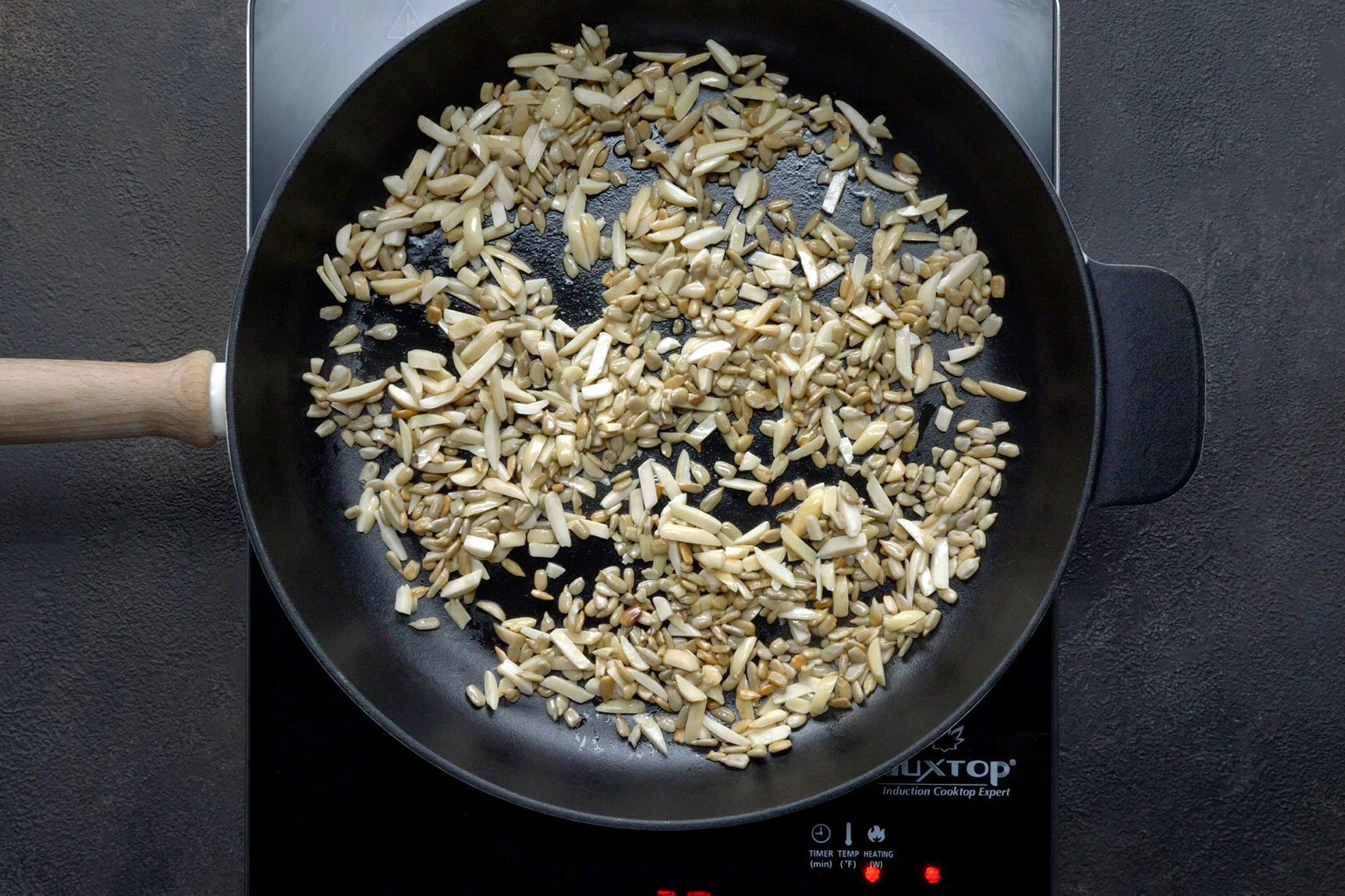 overhead shot; dark grey textured background; In a large skillet, heating 1 tablespoon oil over medium heat; Added almonds and sunflower kernels; cooking until toasted;