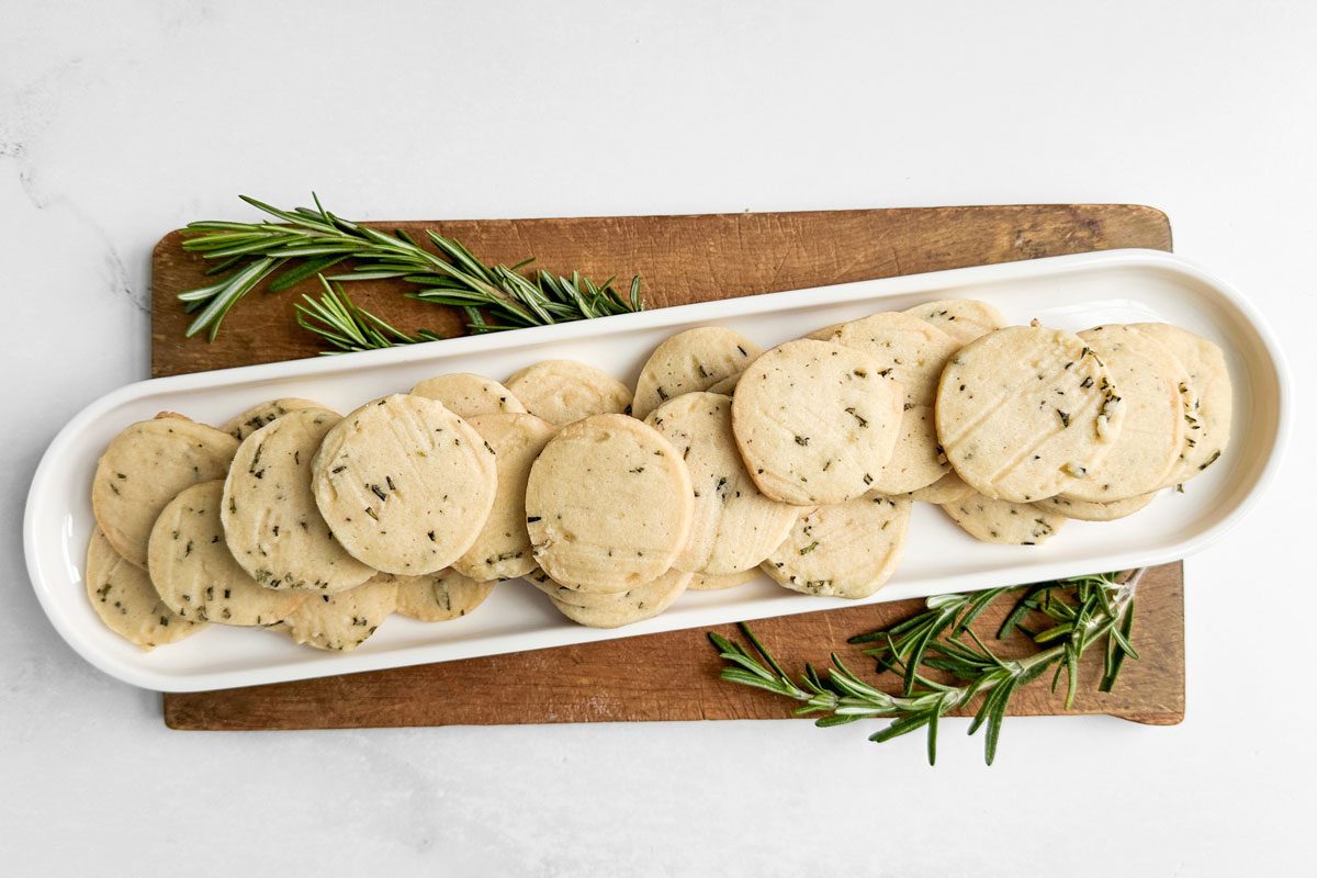 Taste of Home Rosemary Shortbread Cookies on a white tray on a wooden board with sprigs of rosemary