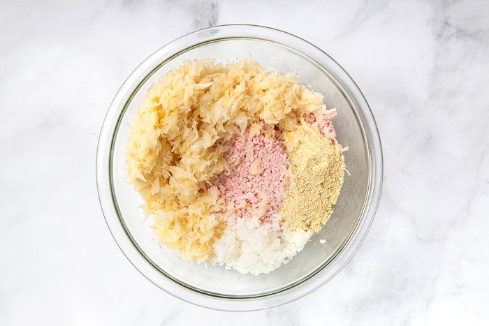 Ground ham, sauerkraut, onion, and breadcrumbs in a mixing bowl for step one of Sauerkraut Balls recipe for Taste of Home