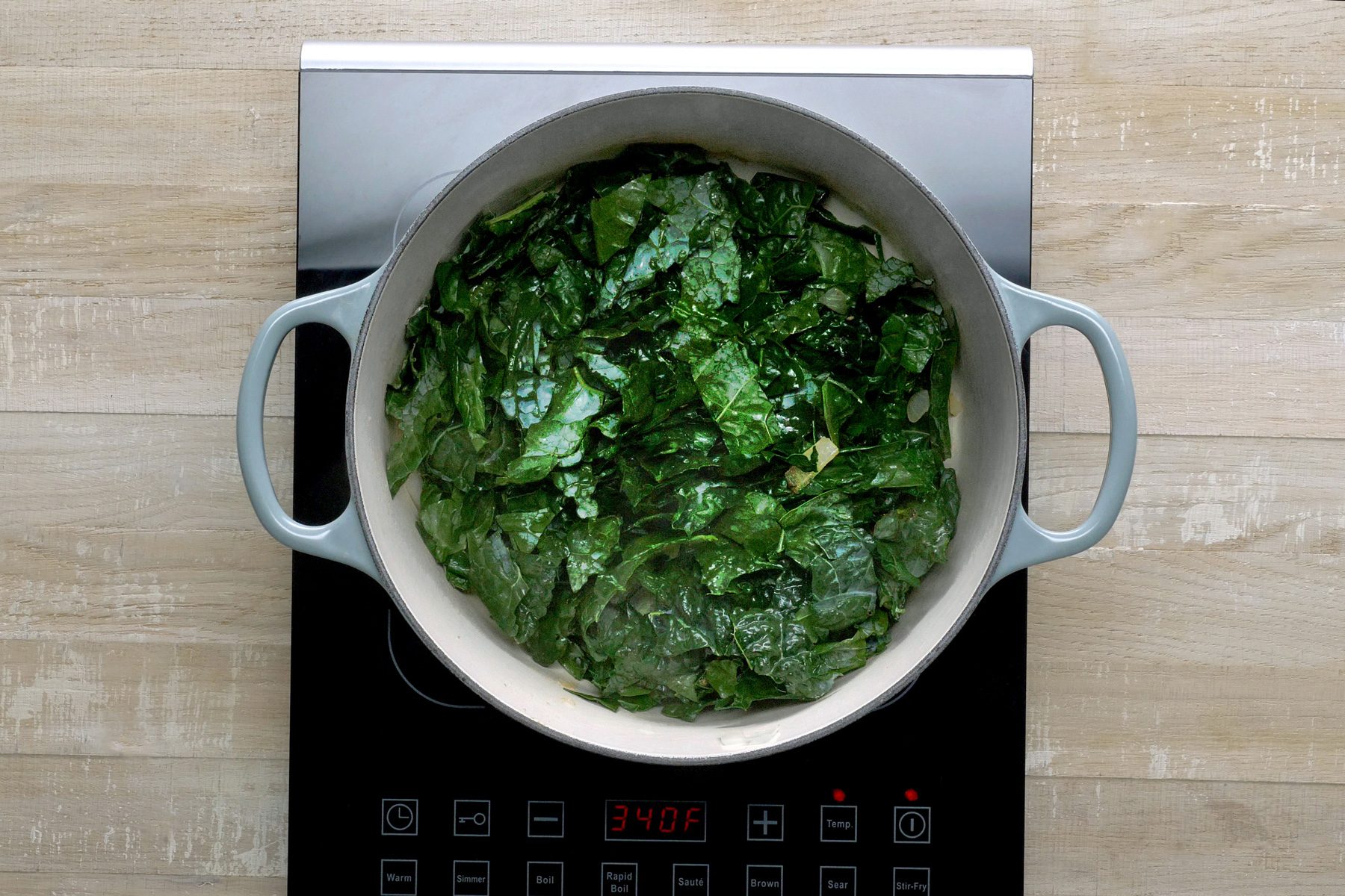 Overvead shot of the same stockpot; add kale to pot; cook and stir 2 minutes; induction; wooden background
