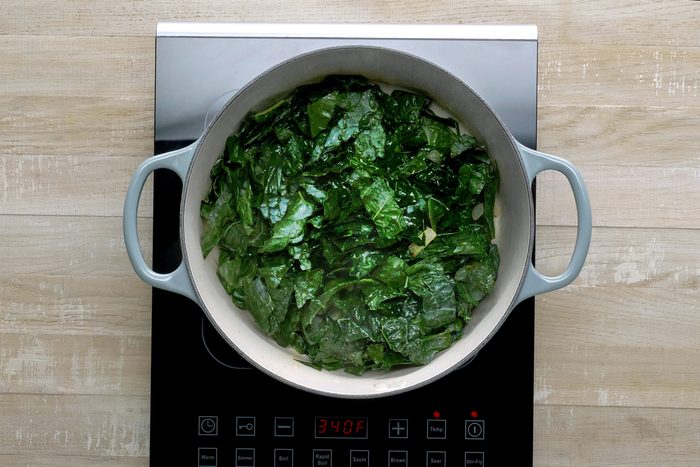 Overvead shot of the same stockpot; add kale to pot; cook and stir 2 minutes; induction; wooden background
