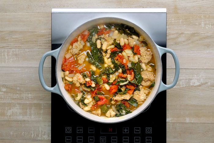 Overhead shot of pot; bring to a boil; reduce heat; simmer, covered until kale is tender; induction; wooden background