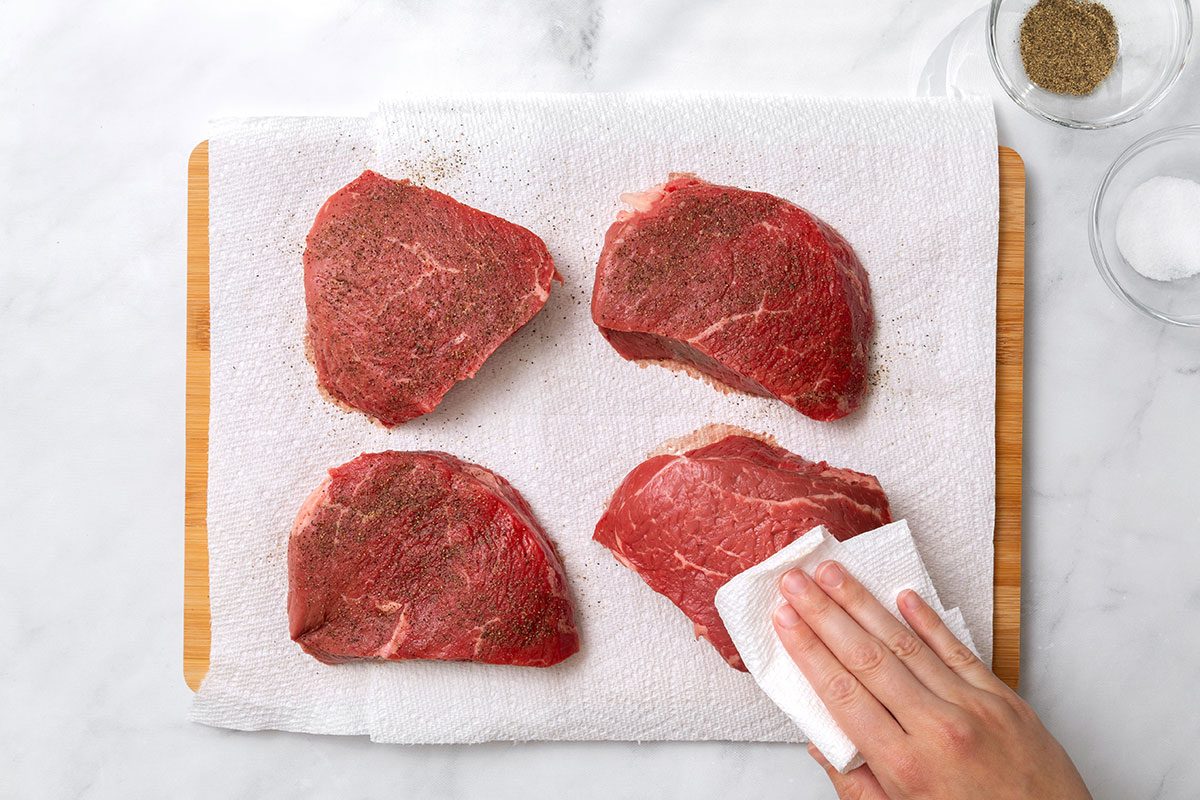 Four top sirloin steaks seasoned and dried on a wooden board for step one for Steak Pizzaiola recipe for Taste of Home