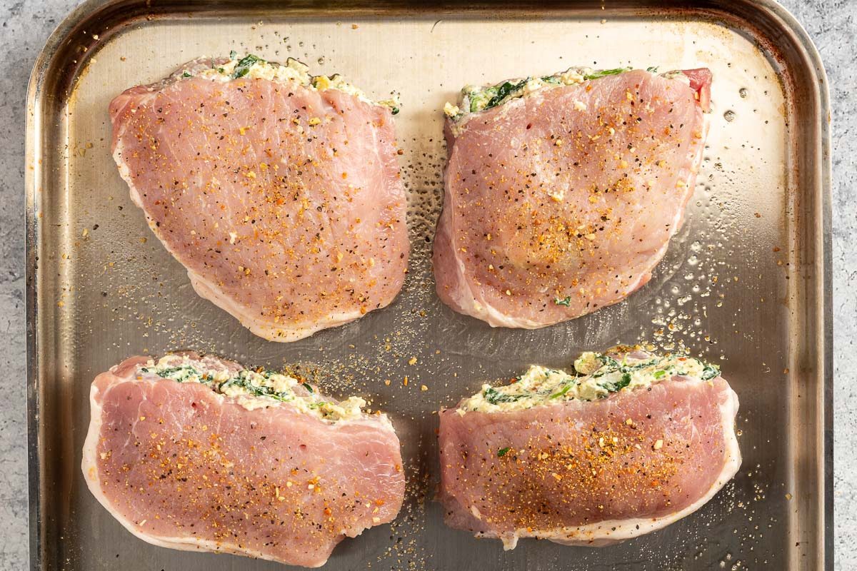 Taste of Home Stuffed Pork Chops photo of the pork chops topped with lemon pepper seasoning on a baking sheet.