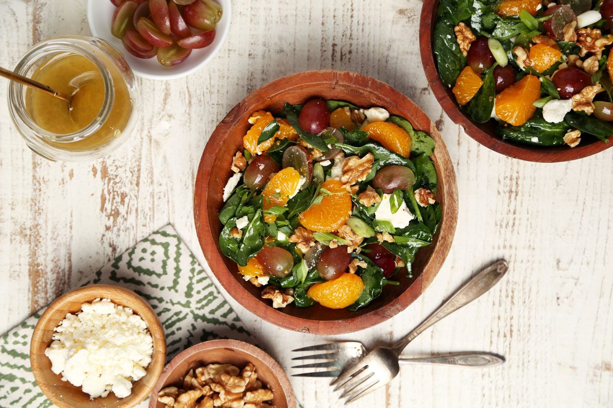 Close up of Taste of Home's Spinach Fruit Salad served in wooden bowls on a white wooden surface with a green towel.
