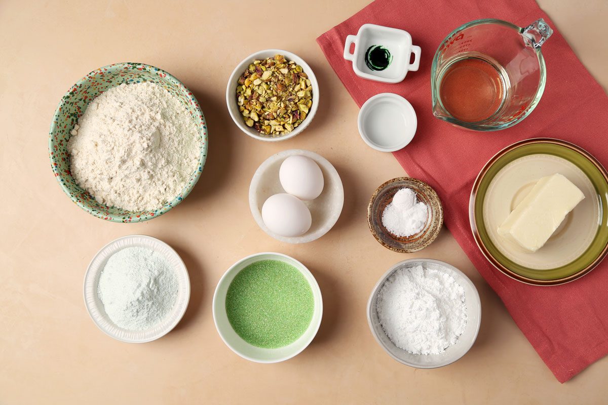 Ingredients for Taste of Home's Pistachio Cookies laid out in small bowls on a pink surface with a pink towel.