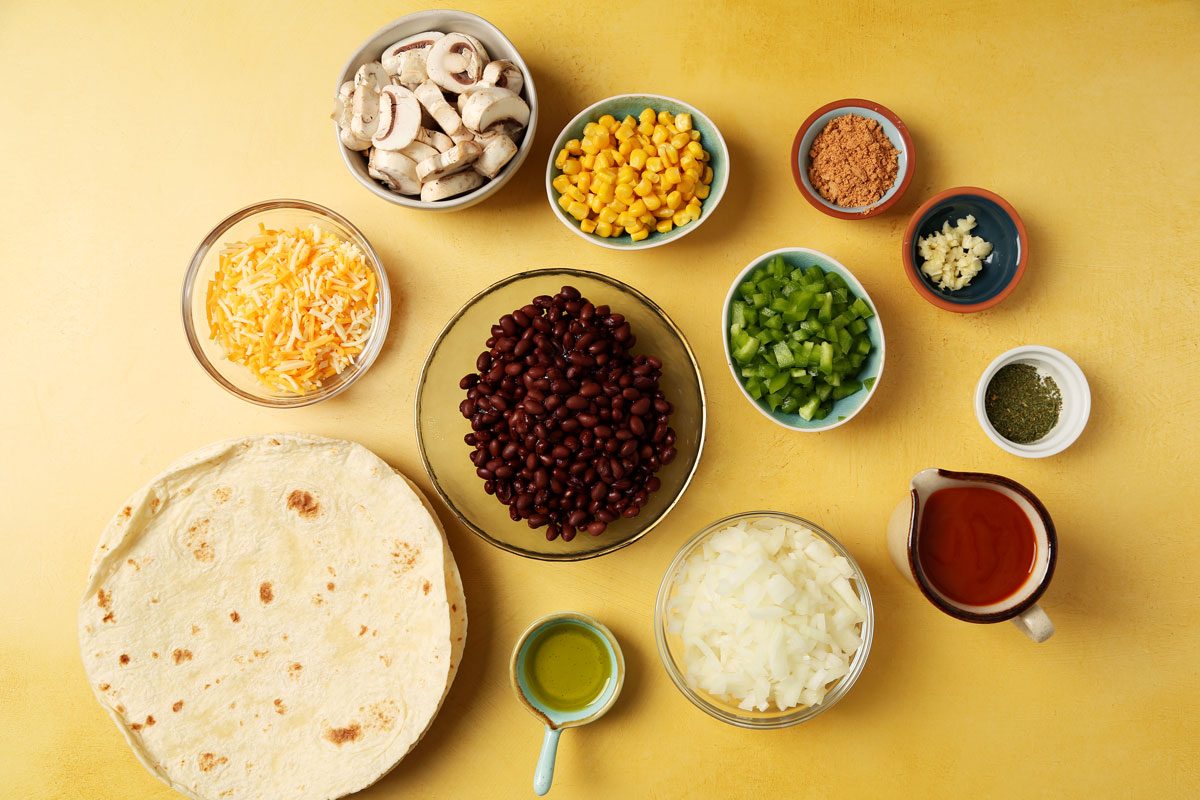 Ingredients for Taste of Home's Vegetarian Enchiladas laid out in small bowls on a yellow surface.