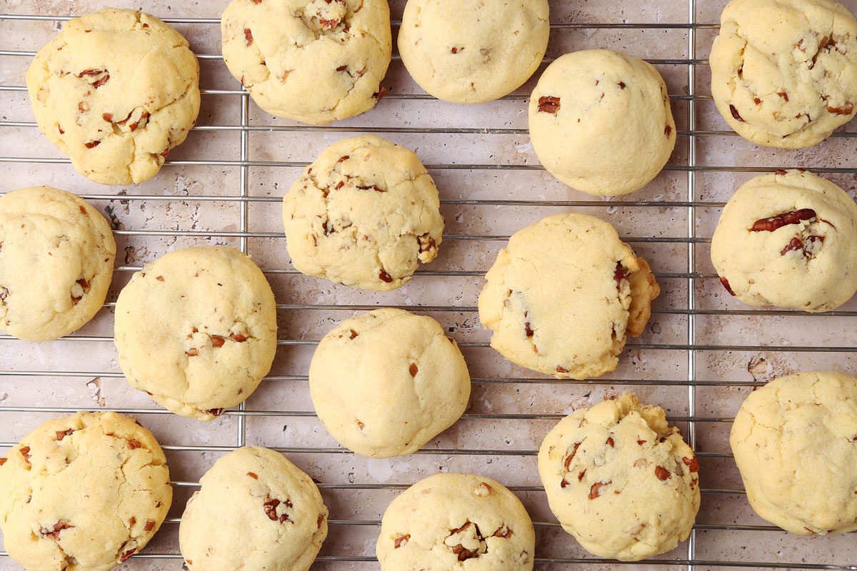 Taste of Home's Butterscotch Cookies on a wire rack with milk on the side and a small bowl of pecans.