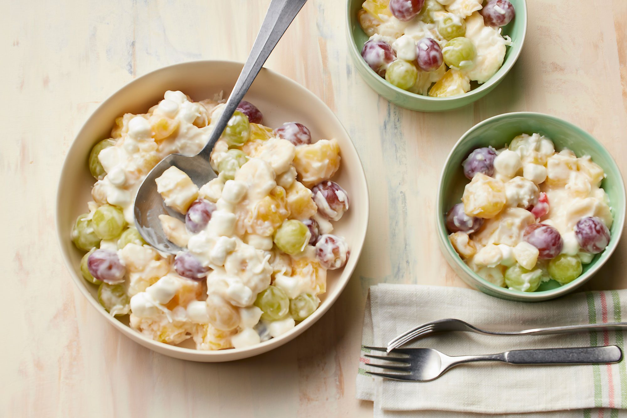 overhead shot of a creamy fruit salad, known as Ambrosia, is showcased in a large bowl placed over wooden background, The salad is a vibrant mix of colorful fruits,