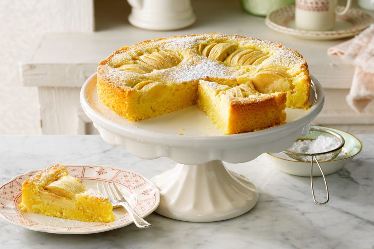 Apfelkuchen on a cake stand with one slice served on a plate nearby