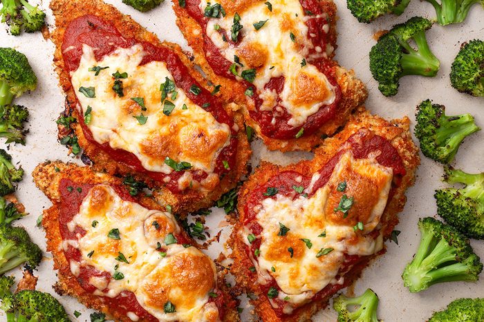 Overhead shot of Baked Chicken Parmesan on a baking pan with roasted broccoli florets