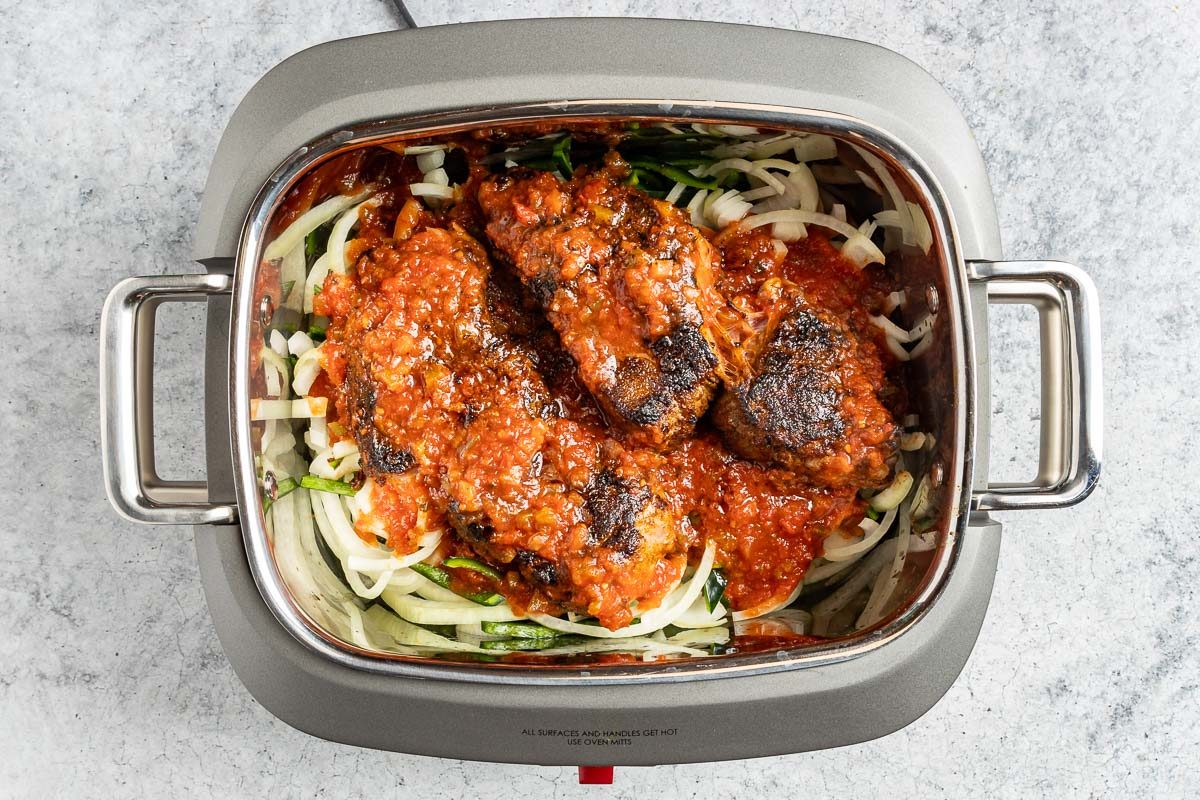 Taste of Home Beef Carnitas photo of the onion, poblano peppers and brown chuck roast in a slow cooker.