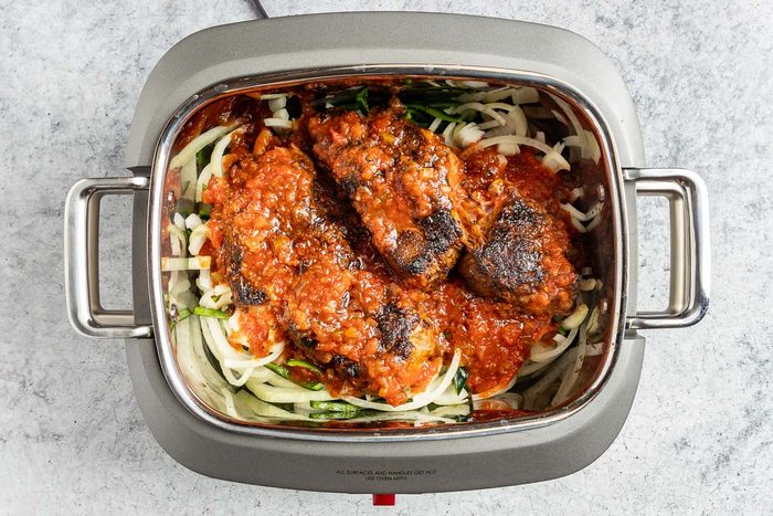 Taste of Home Beef Carnitas photo of the onion, poblano peppers and brown chuck roast in a slow cooker.