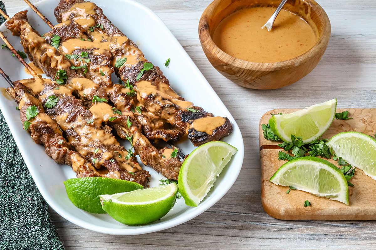 Beef satay with peanut sauce, lime wedges, and cilantro.