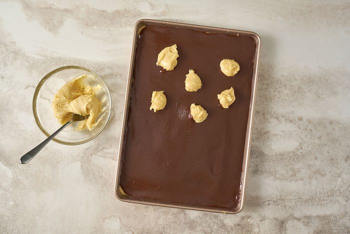 Taste of Home Cake Mix Bars: The final layer of cake mix topping is added over the chocolate filling before baking, showing scoops of cake mix being placed on top.