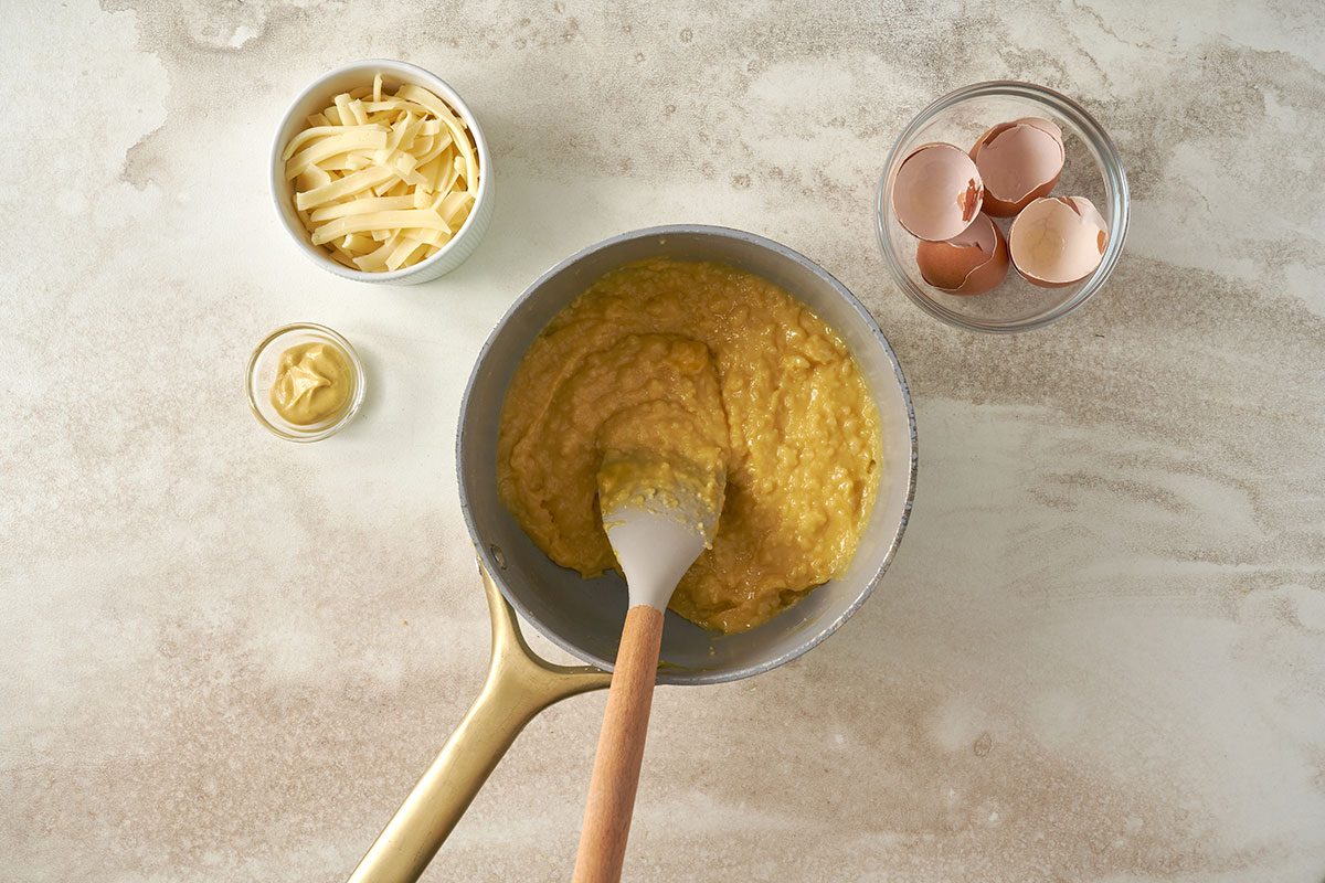 Boiling water, butter, salt, and cayenne, then stirring in flour to form a smooth dough for the Cheese Puffs recipe, by Taste of Home. Beating in eggs and stirring in Gruyere cheese and mustard.
