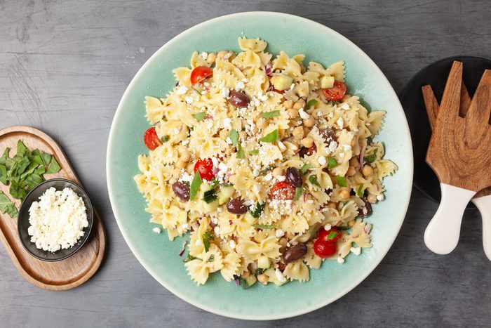 Full yield of Taste of Home Chickpea Pasta Salad in a light blue serving bowl, wooden salad servers, feta and basil