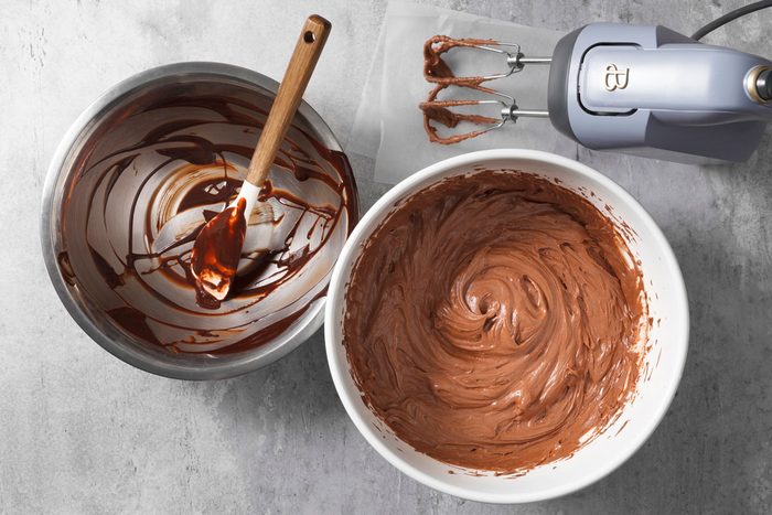 All frosting ingredients combined in a mixing bowl with mixer placed nearby