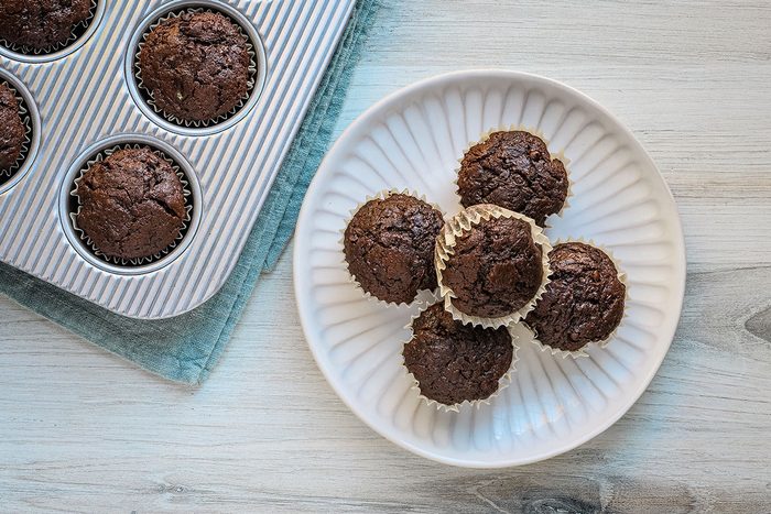 Freshly baked homemade chocolate zucchini muffins on a plate with more in a muffin tin in the background.