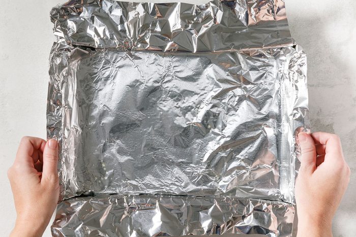 hands lining A 13x9 In. Baking Pan With Foil, Letting Ends Extend Up Sides