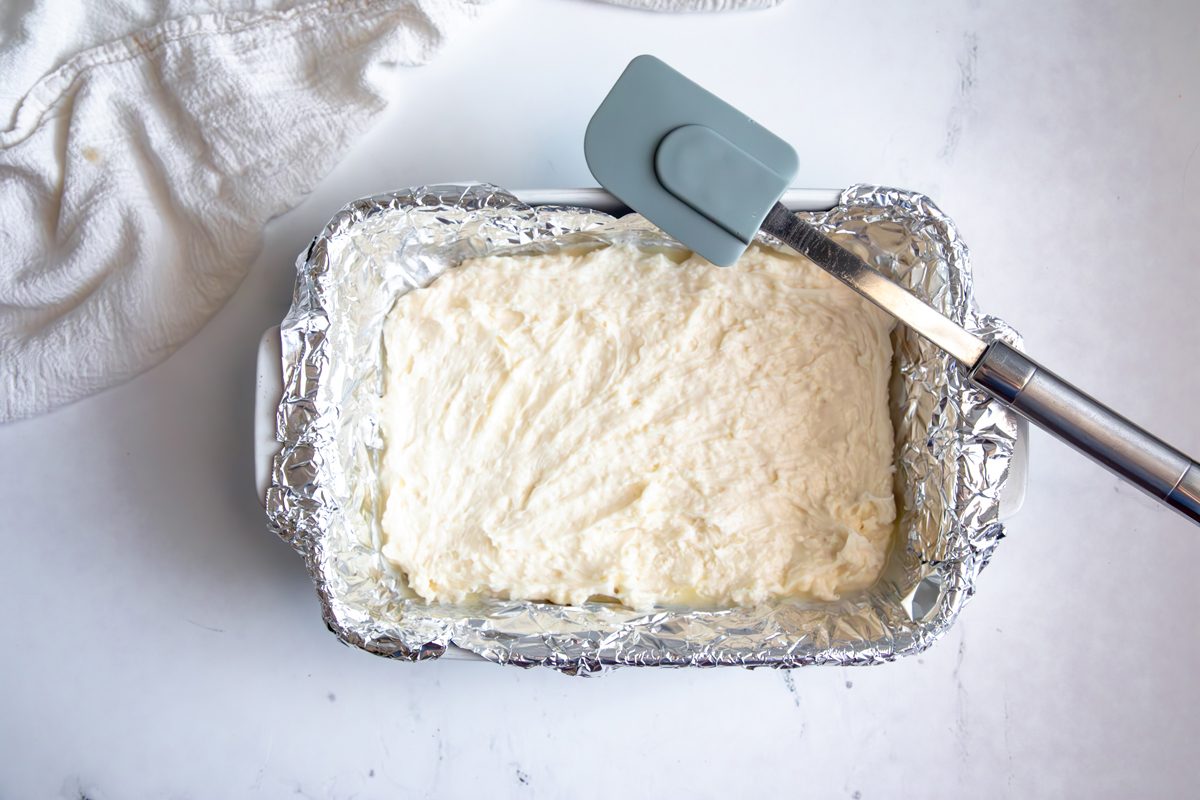 Overhead shot for Taste of Home Coconut Snowballs, coconut snowball mixture pressed into baking dish with tin foil.