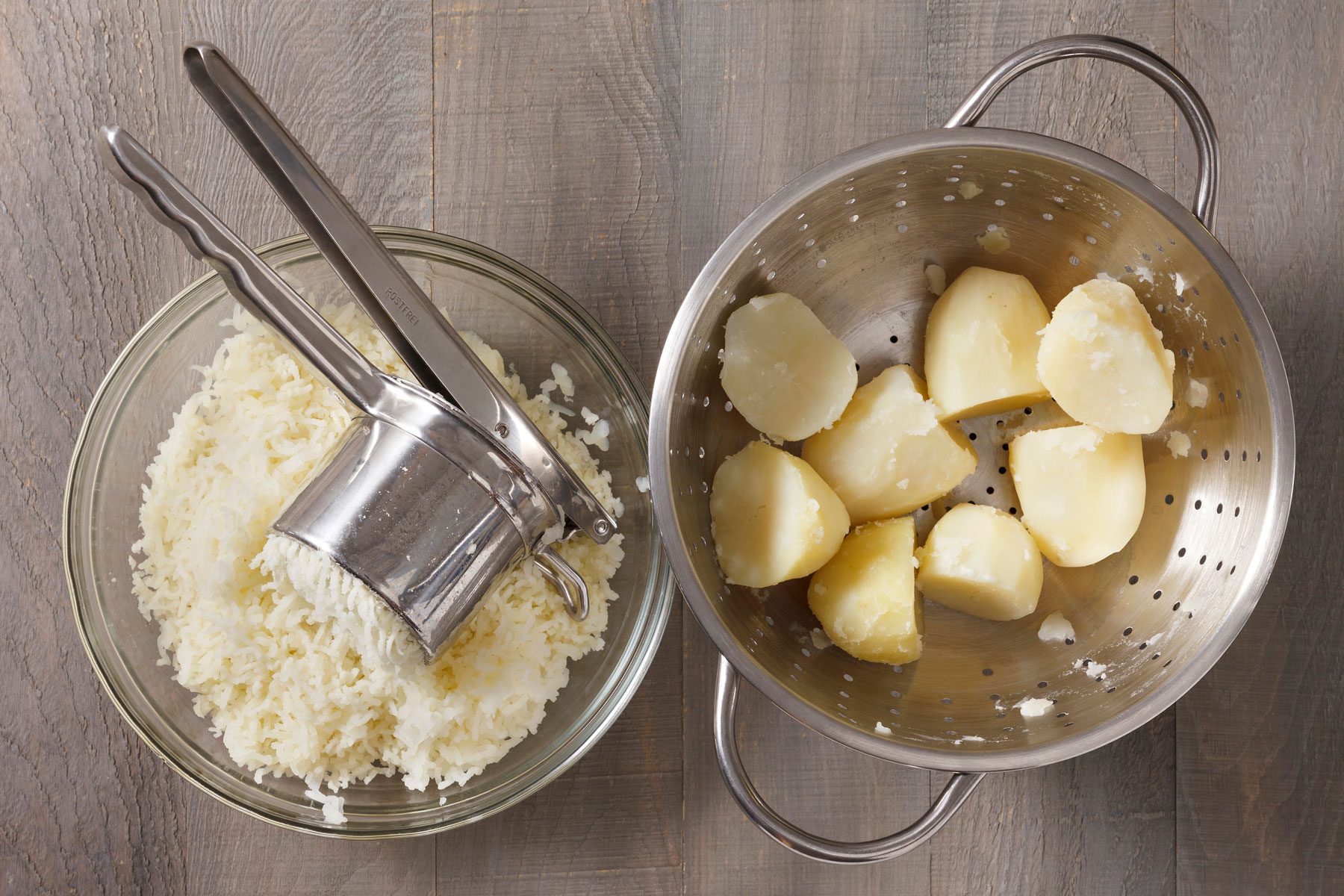 Potatoes pushed through a strainer in a large bowl with boiled potatoes next to it.