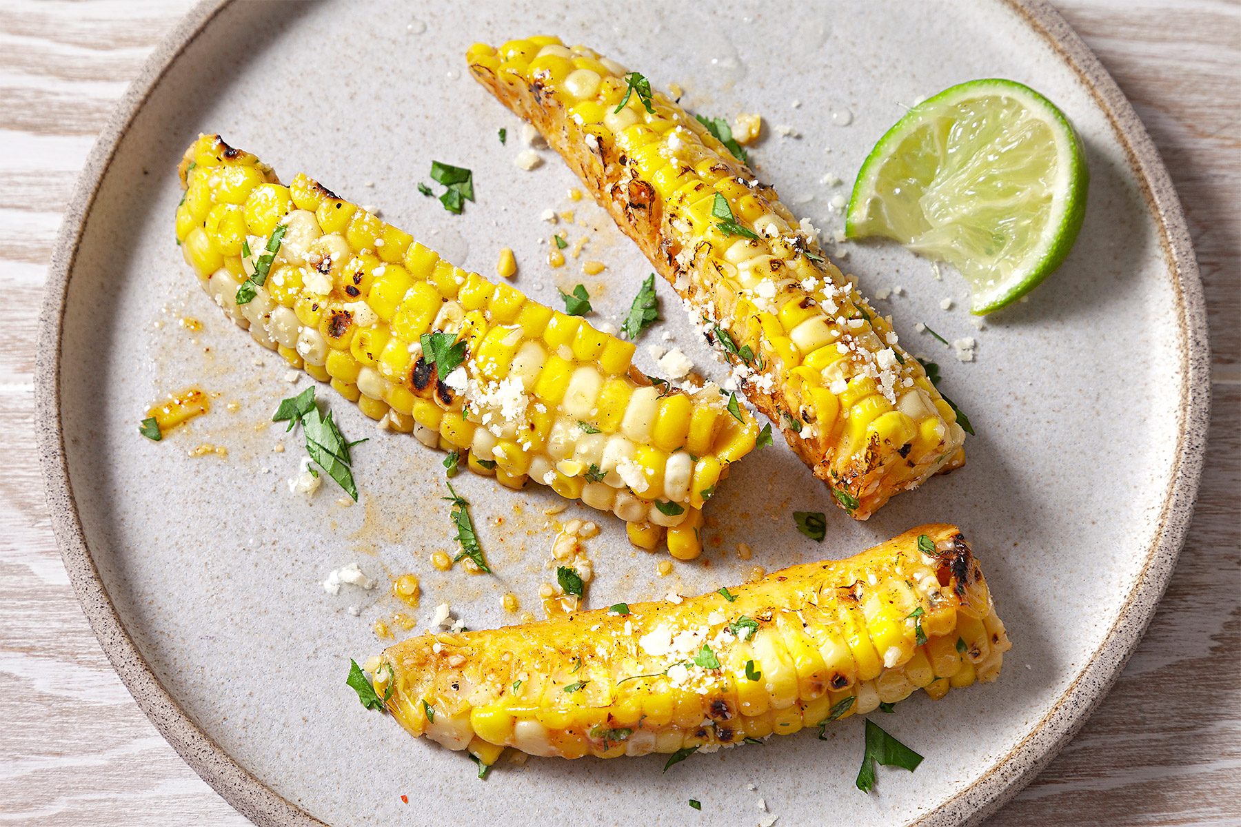 Closeshot of Corn Ribs; sereve on large plate with lime wedges; sprinkle parmesan cheese; wooden surface;