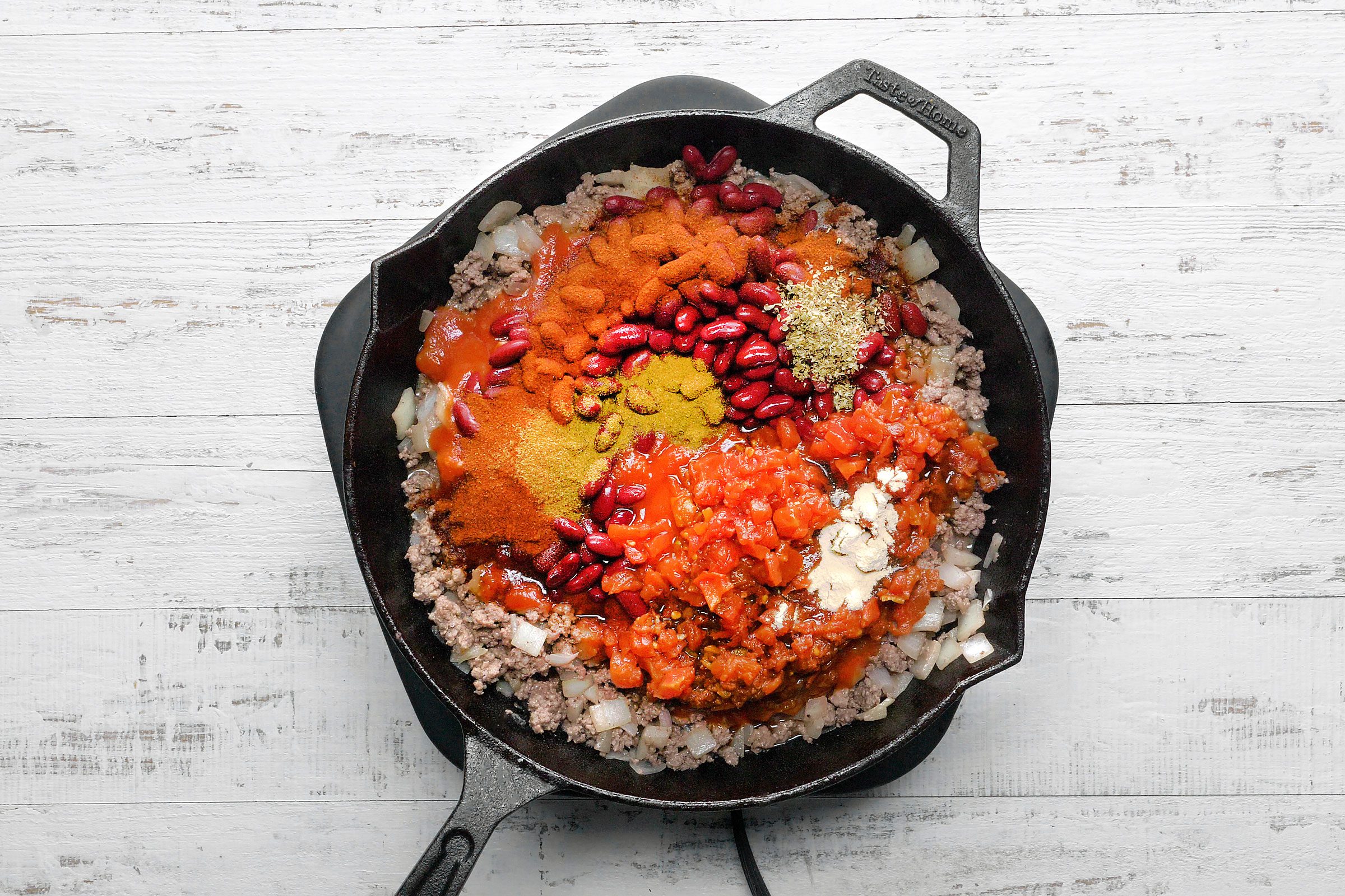 Bacon with beans, tomato sauce, diced tomatoes, chili powder, Worcestershire sauce, cumin, oregano and garlic powder in a skillet
