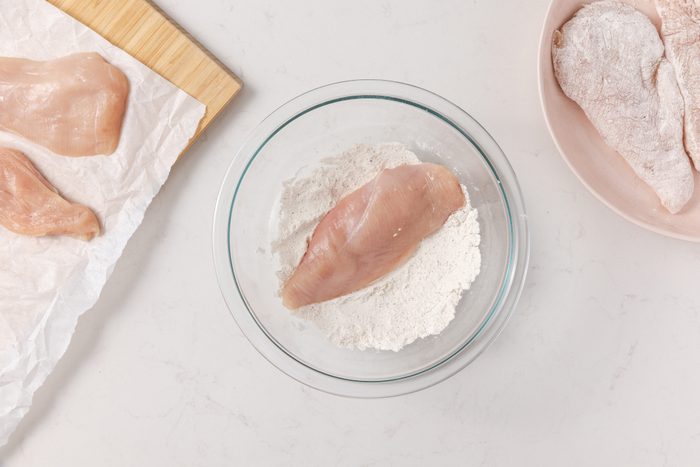 Chicken breast being coated with flour in shalow bowl.