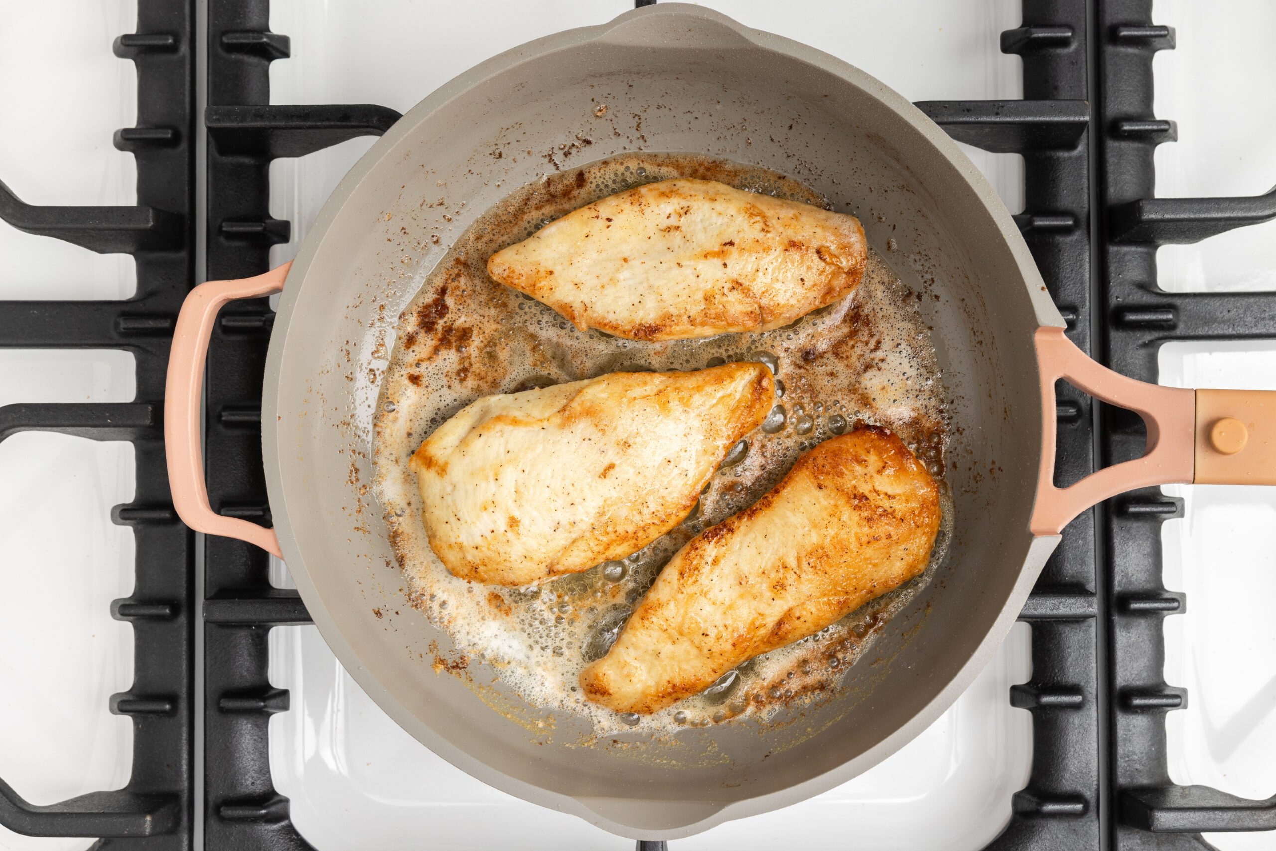 Chicken breasts being cooked in skillet.