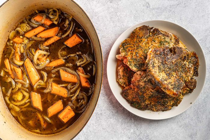 Taste of Home Dutch Oven Pork Chops photo of the seasoned and. browned pork chops with the carrots and broth in the Dutch oven.