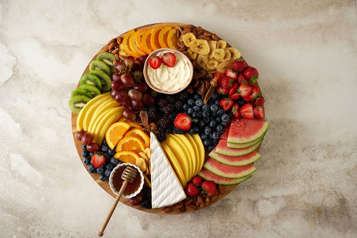 An overhead view of the Fruit and Cheese Platter, showcasing the vibrant fruits, cheeses, and almonds arranged around a jar of honey, by Taste of Home.