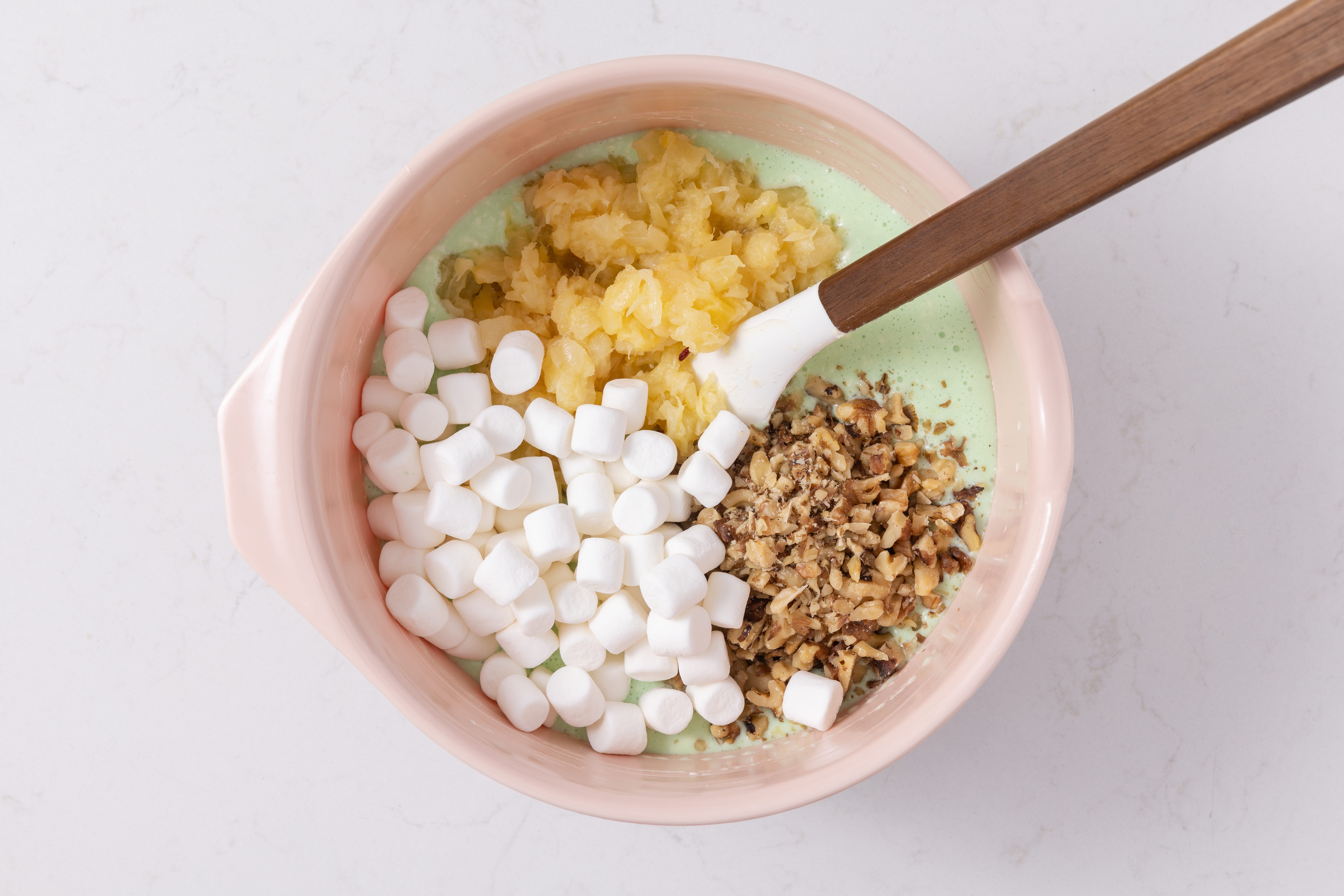 Crushed pineapple, miniature marshmallows and chopped walnuts being combined with gelatin mixture.