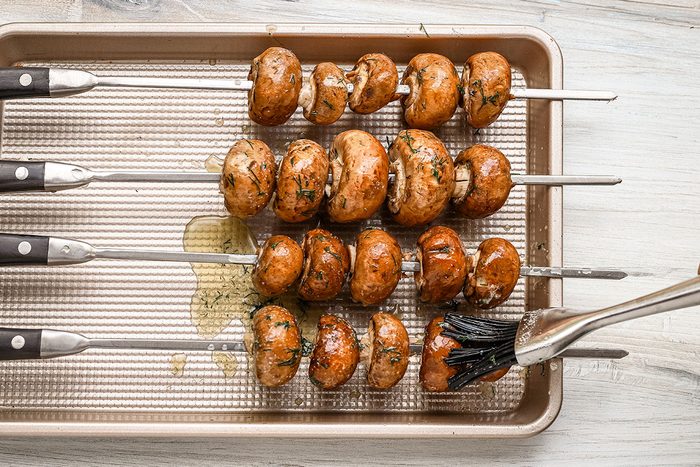 Basting skewered mushrooms with a butter, dill, and garlic mixture.
