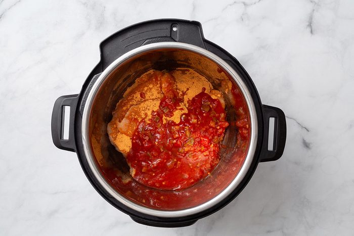 Taco seasoning sprinkled over chicken breasts and topped with salsa in a pressure cooker for step one of Instant Pot Salsa Chicken recipe for Taste of Home