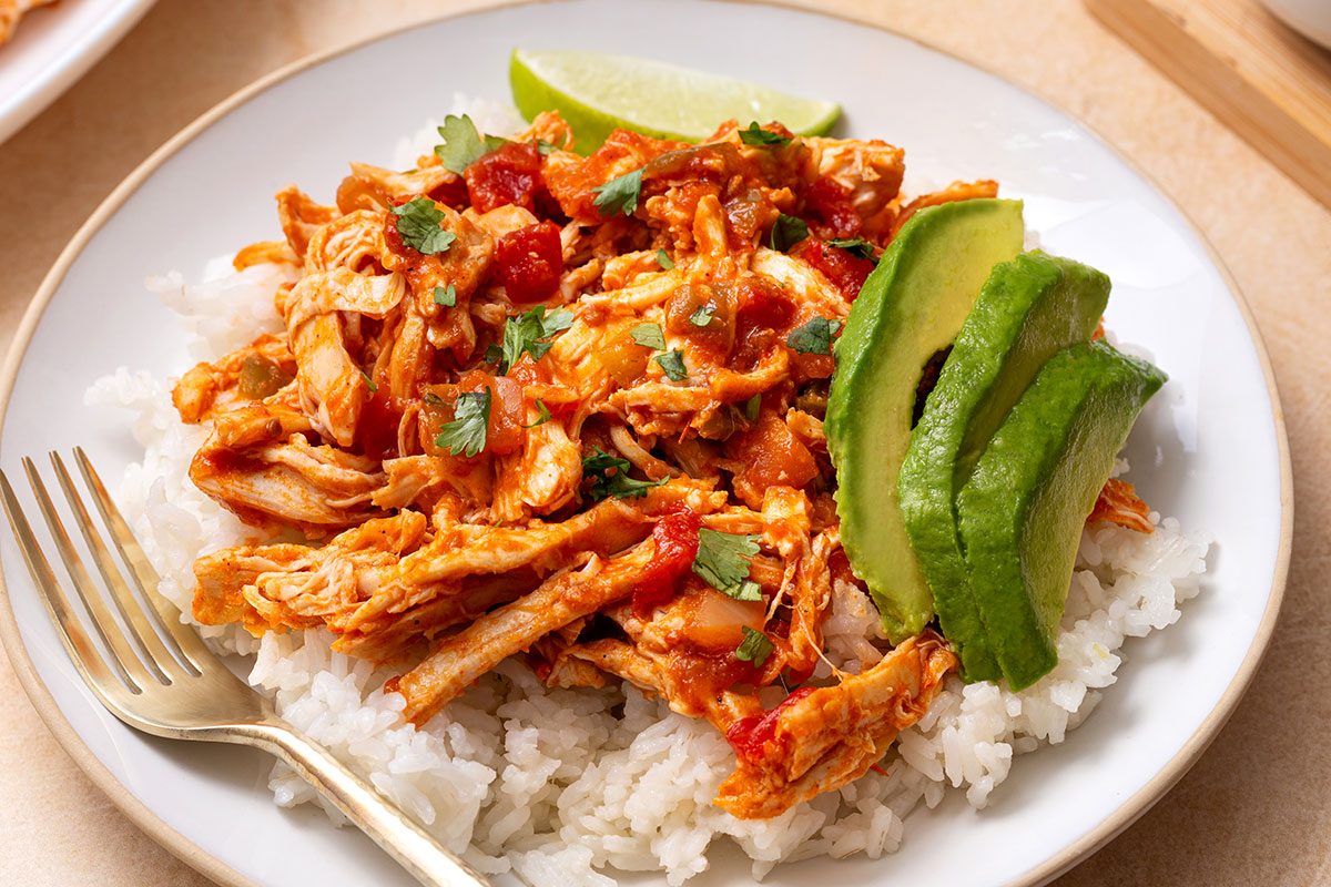 Instant Pot Salsa Chicken served on top of rice with cilantro, lime wedges and avocado slices for Taste of Home