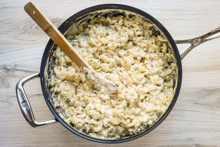 A large saucepan with macaroni being stirred into the cheese sauce for a meal of baked jalapeno mac and cheese.