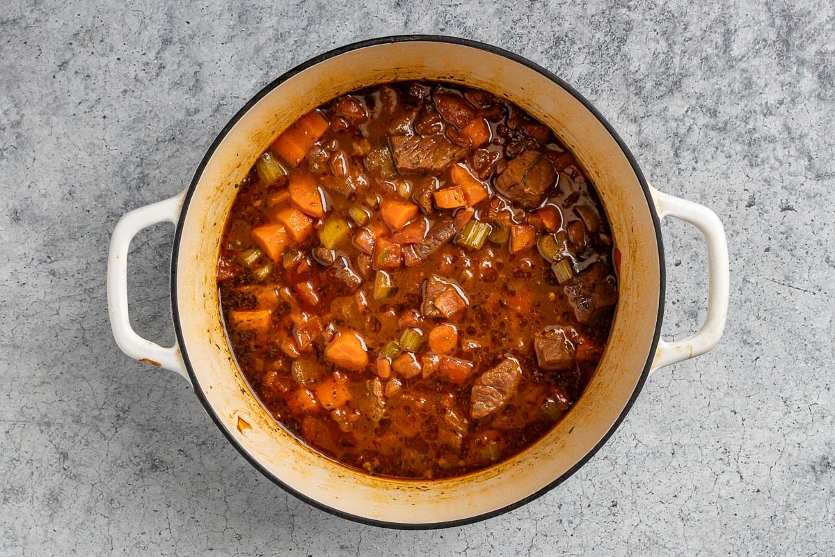 adding the vegetables, broth, barbecue sauce, soy sauce, steak sauce and seasoning to the Dutch oven.