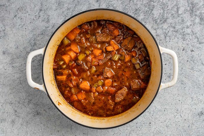 adding the vegetables, broth, barbecue sauce, soy sauce, steak sauce and seasoning to the Dutch oven.