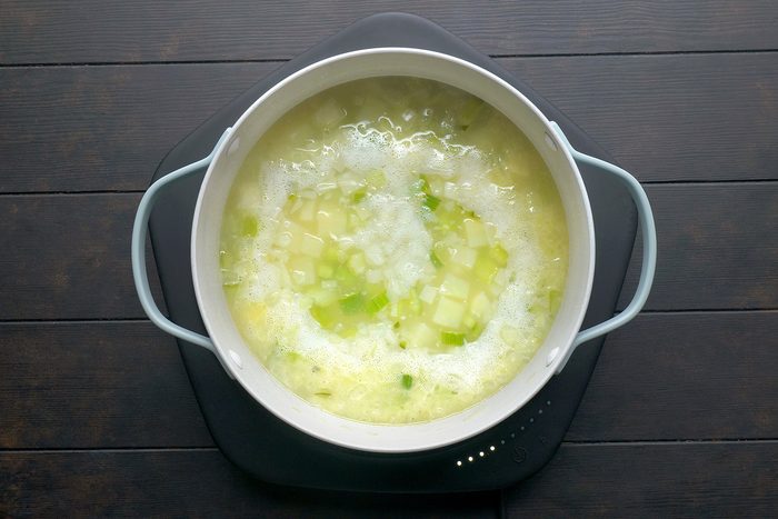 A pot of bubbling soup on a dark wooden surface, featuring diced potatoes and green vegetables in a creamy broth.